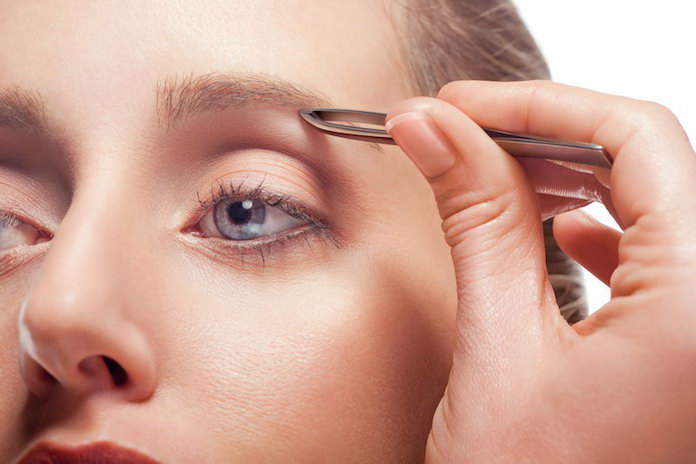 Close-up of woman plucking eyebrow using tweezers