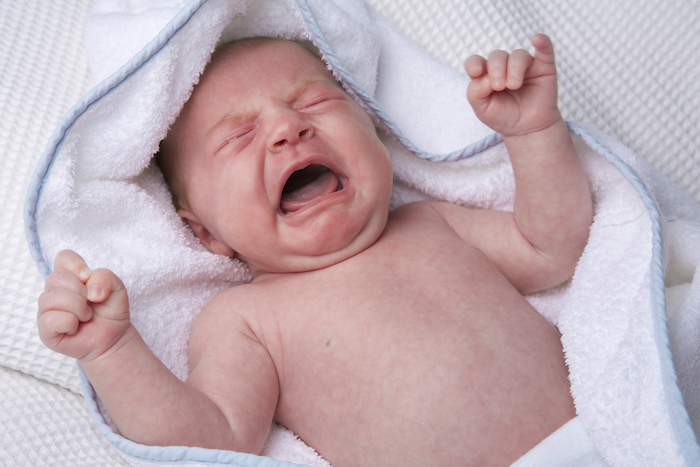 A crying newborn in a white towel.